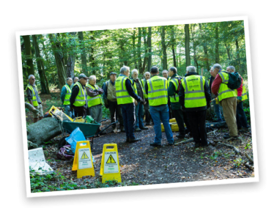 A bout a dozen volunteers with high visibility vests meeting in the woods