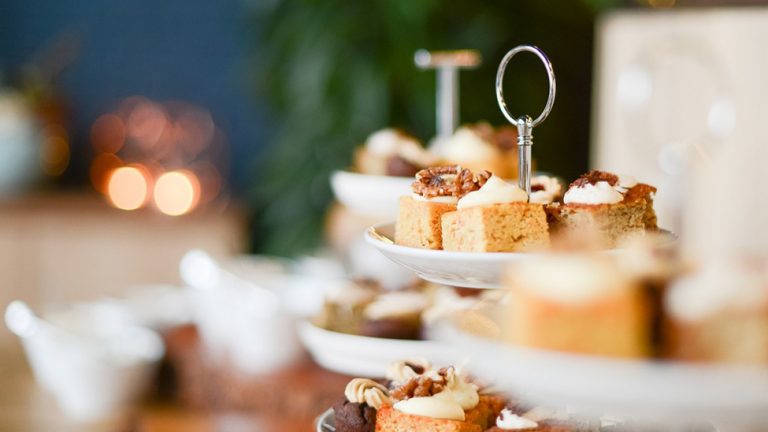 Small cakes on a cake stand with teapots in the background